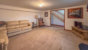 Una sala de estar con alfombra color beige, un sofá de cuero, una silla de madera, una lámpara y un televisor sobre un mueble de madera.