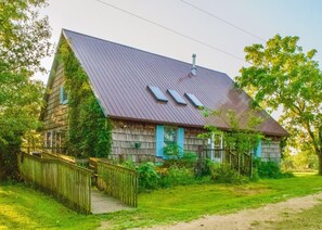 A rustic wooden house with a sloped roof, a wooden fence, and a pathway leading to the entrance.
