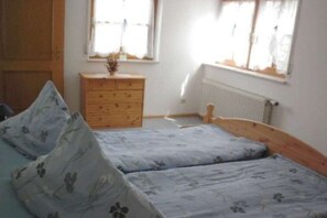 Une chambre avec deux lits simples, une commode en bois et une fenêtre avec des rideaux.