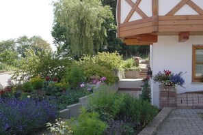 A white building with a wooden gable roof and a garden with various plants and flowers. - Holiday apartment with 1 bedroom (St. Peter)