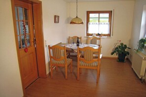 A dining area with a wooden table and chairs, a hanging light fixture, a window with curtains, and a potted plant. - Holiday apartment with 1 bedroom (St. Peter)