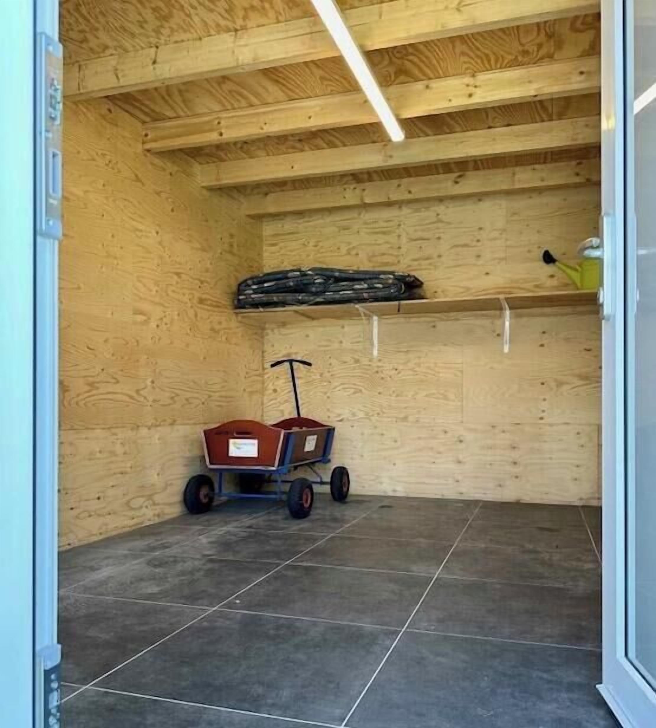 Una habitación con techo de madera, suelo de baldosas y un carrito rojo con ruedas.