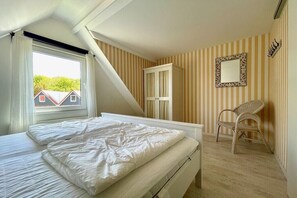 Ein Schlafzimmer mit Bett, Fenster, Sessel und Kleiderschrank.