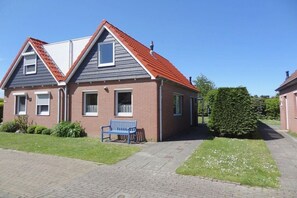 Ein zweigeschossiges Wohnhaus mit rotem Ziegeldach, einer Ziegel-Fassade und einer blauen Bank im Vordergrund.