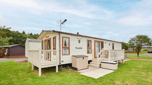 A mobile home with a porch, a deck, and a small outdoor seating area.