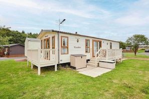 A mobile home with a porch, a deck, and a small outdoor seating area.