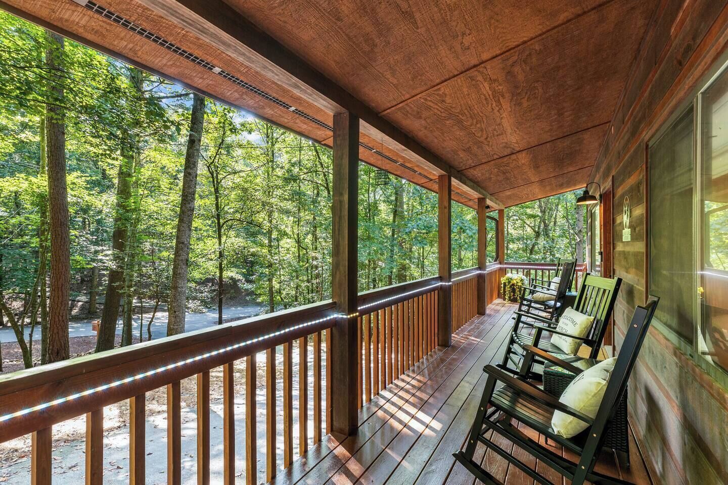 A wooden deck with a railing, chairs, and a view of a forest.
