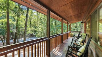 A wooden deck with a railing, chairs, and a view of a forest.