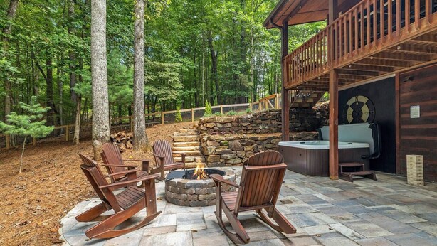 A patio with a stone fire pit, wooden chairs, and a hot tub. - River Resort | Hot Tub + Game Room + Fenced Yard (Ellijay)
