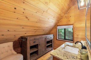 L’intérieur d’une cabane en bois, avec un meuble en bois, un banc, un évier et une fenêtre donnant sur les arbres.