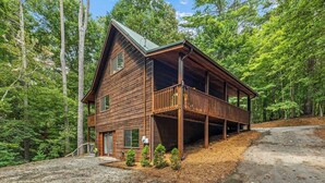 A cabin with a wooden exterior, a balcony, and a gravel driveway. - River Resort | Hot Tub + Game Room + Fenced Yard (Ellijay)