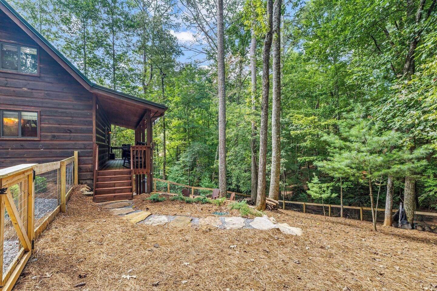 A wooden cabin with a deck and a fenced yard.