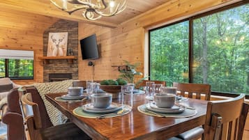 A wooden dining room with a large table set for six, a stone fireplace, and a television mounted on the wall.
