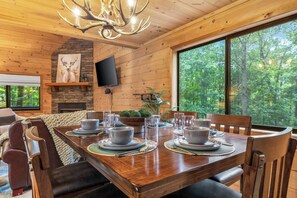 Ein Esszimmer mit Holzboden, einem großen Esstisch für sechs Personen, einem Kamin aus Stein und einem an der Wand befestigten Fernseher.