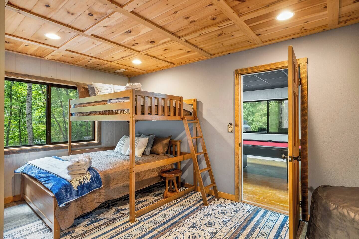 A bunk bed with a ladder, a window with a view of trees, and a patterned rug.
