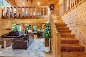 Een houten chalet van binnen met een woonkamer, keuken en een trap.