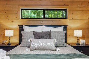 Een bed met meerdere kussens, een raam erboven en twee nachtkastjes met lampen.