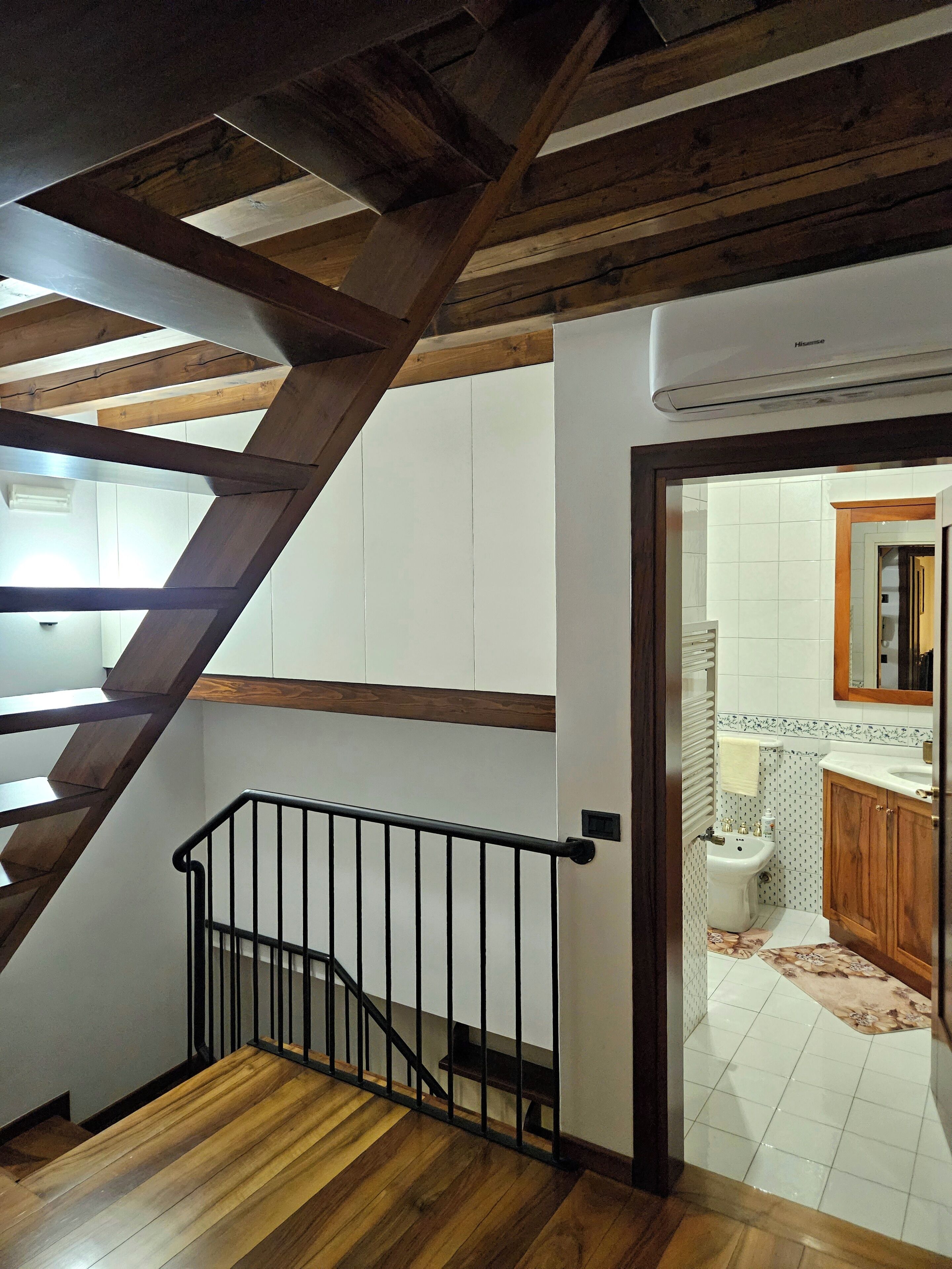 Un escalier en bois avec une rampe noire menant à une salle de bain dotée d’un lavabo blanc et d’armoires en bois.