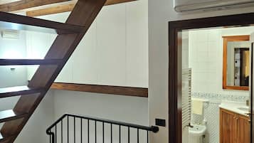 Un escalier en bois avec une rampe noire menant à une salle de bain dotée d’un lavabo blanc et d’armoires en bois.