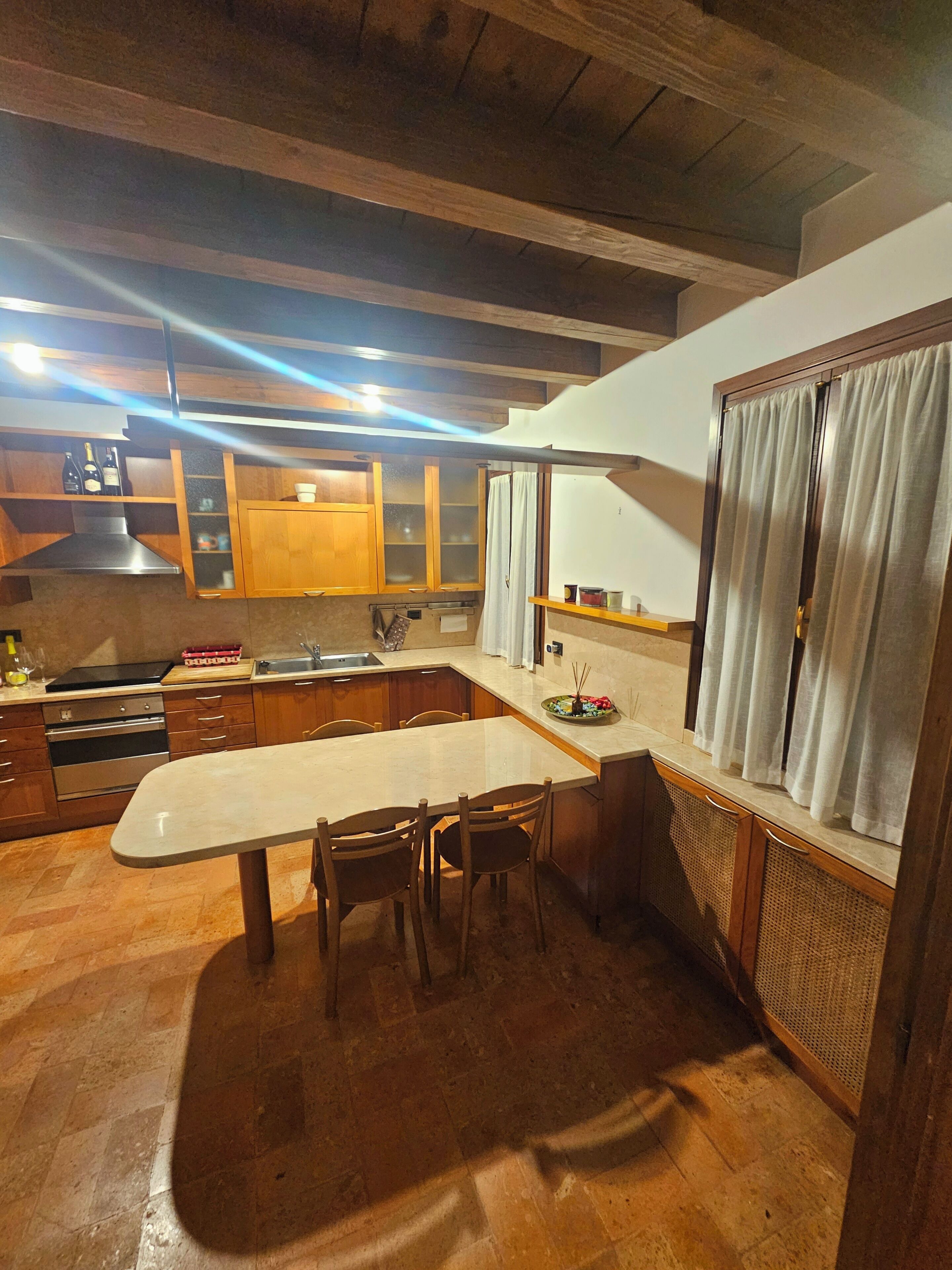 Une cuisine avec des meubles en bois, un plan de travail en marbre et un coin repas avec des chaises.