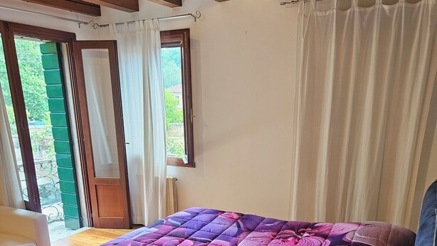 Makuuhuone, jossa on sänky, puulattia, ikkuna verhoilla ja näkymä vehreään maisemaan.