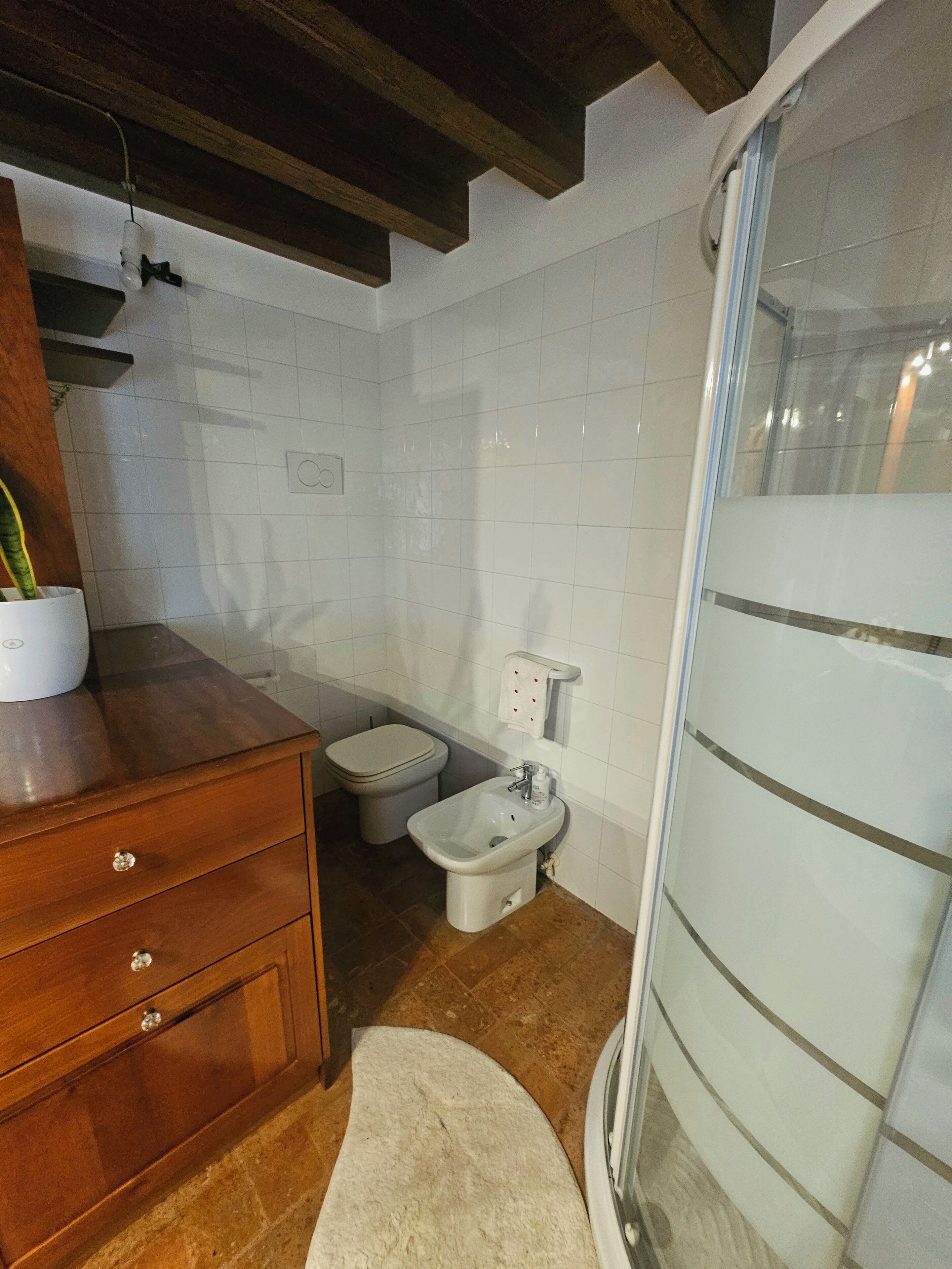 Une salle de bain avec un meuble-lavabo en bois, des toilettes, un bidet et une douche à parois de verre.