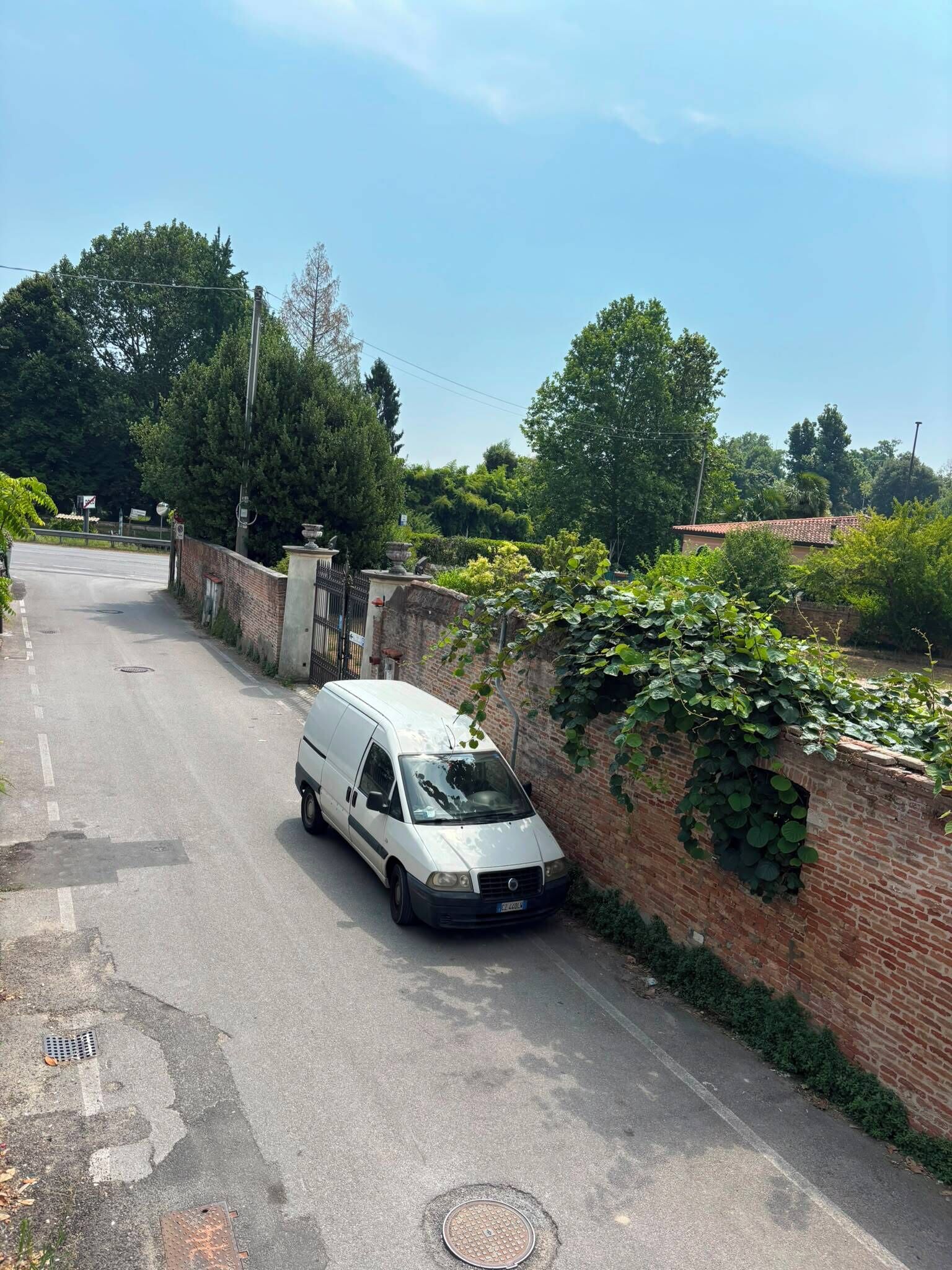 Un fourgon blanc était garé sur une route asphaltée, avec un mur de briques d’un côté et un portail en métal de l’autre.
