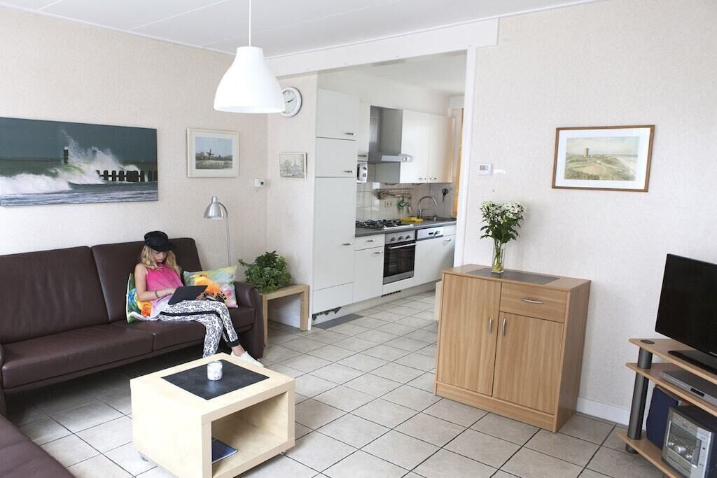 A living room with a sofa, coffee table, and a television. There is a kitchen area with cabinets and a stove.