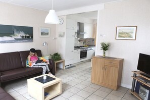 A living room with a sofa, coffee table, and a television. There is a kitchen area with cabinets and a stove. - Holiday home in Domburg with swimming pool (domburg)