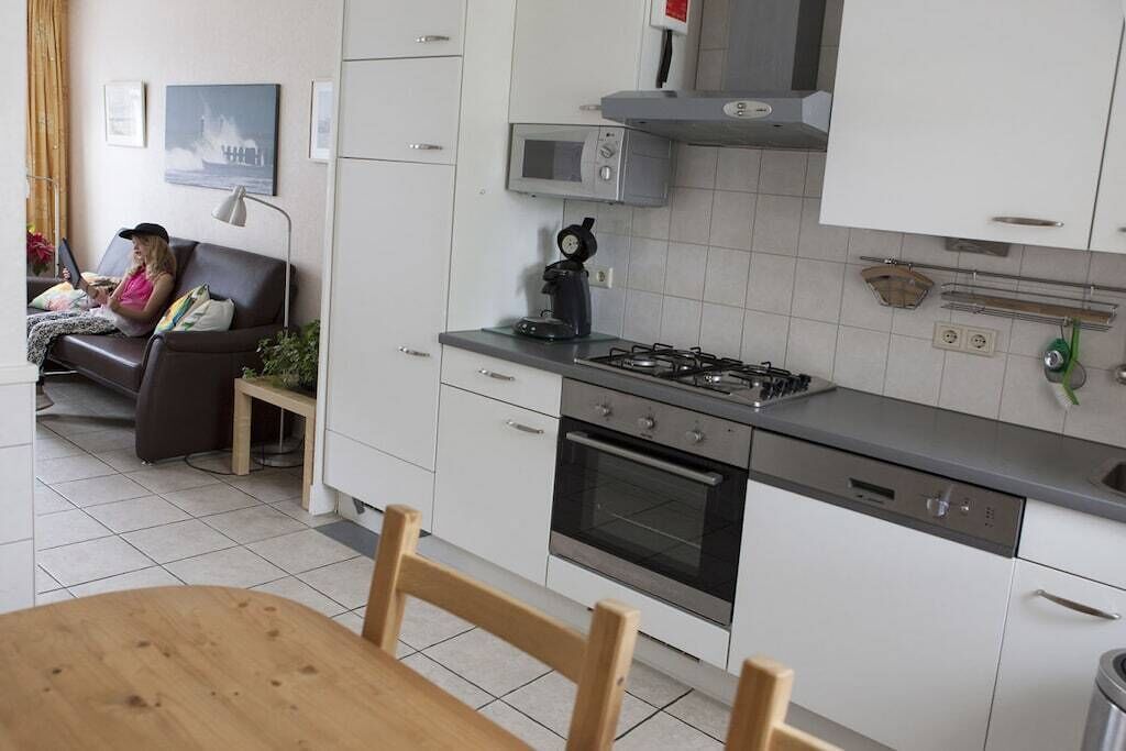 Moderni keittiö, jossa on valkoiset kaapit, kaasuliesi, uuni ja mikroaaltouuni. Etualalla on ruokapöytä ja tuolit.