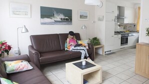 A living room with a brown sofa, a small wooden coffee table, and a painting of a seascape on the wall. - Holiday home in Domburg with swimming pool (domburg)
