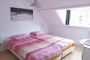 Een slaapkamer met een bed, een raam, een nachtkastje en een aan de muur hangend schilderij.