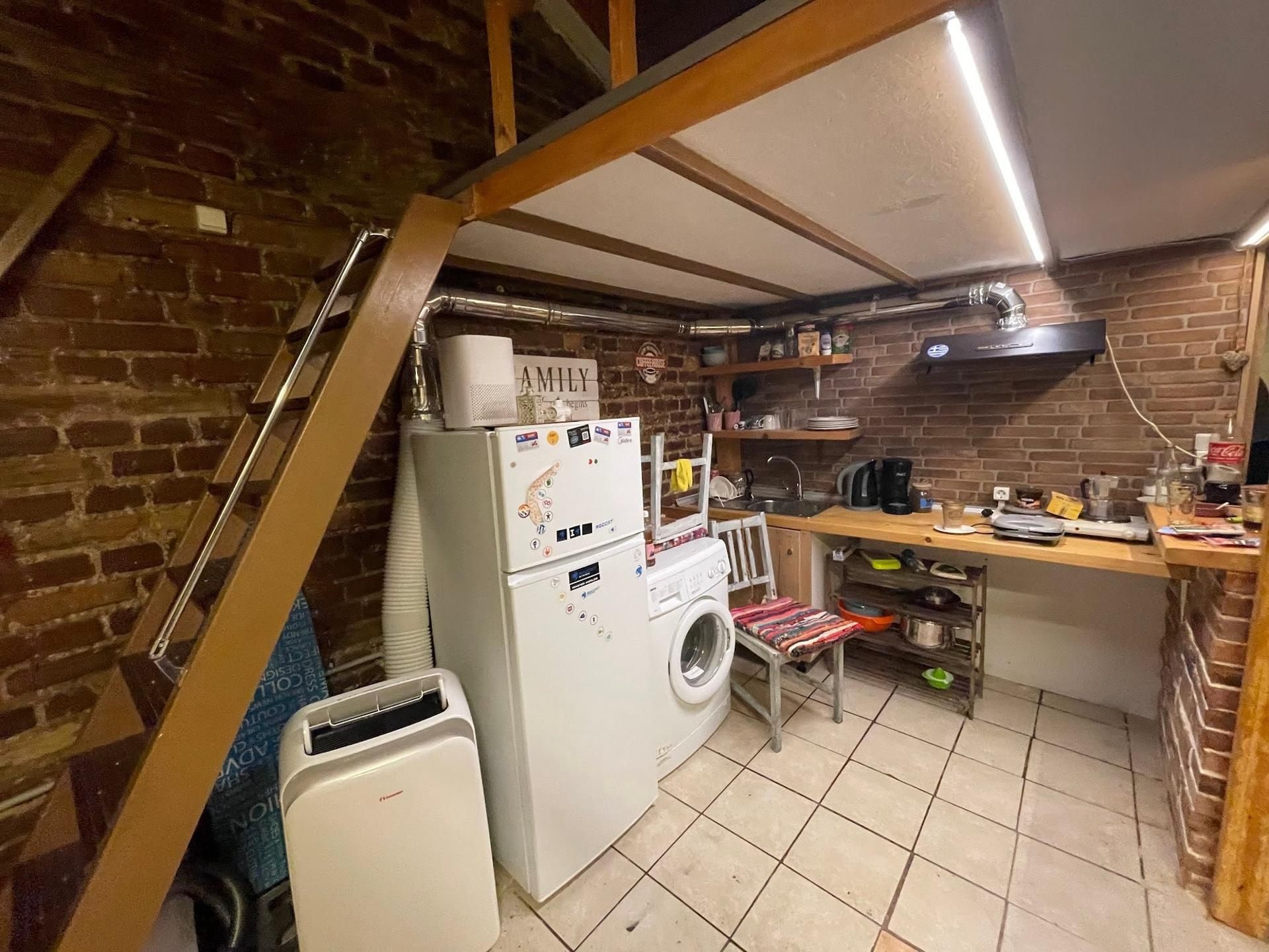 Een kleine keuken met een wasmachine, een tafeltje en een stoel.