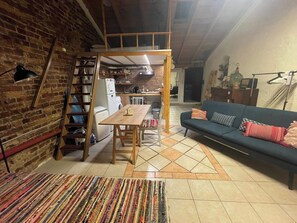 Uma sala de estar acolhedora com um sofá, uma mesa de jantar e uma área de cozinha ao fundo.