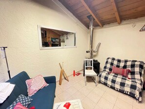 Uma sala de estar com um sofá azul, um sofá xadrez, uma cadeira de madeira, uma janela e uma lareira.