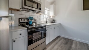 Cozinha moderna com armários brancos, eletrodomésticos de aço inoxidável e piso de madeira.