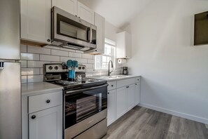 A modern kitchen with white cabinetry, stainless steel appliances, and a wooden floor. - Cottage on Historic Rt. 66 Moonstone (El Reno)