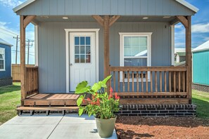 A covered porch with a bench, a potted plant, and a door leading to a building.