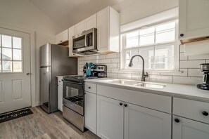 A modern kitchen with stainless steel appliances, white cabinetry, and a large window providing natural light.