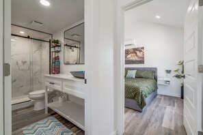 A modern bathroom with a glass shower enclosure, a toilet, and a vanity with a mirror and towel rack. - Cottage on Historic Rt. 66 Moonstone (El Reno)