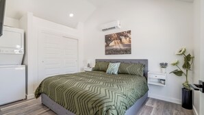 Quarto com cama, mesa de cabeceira, ar-condicionado fixado na parede e uma porta.