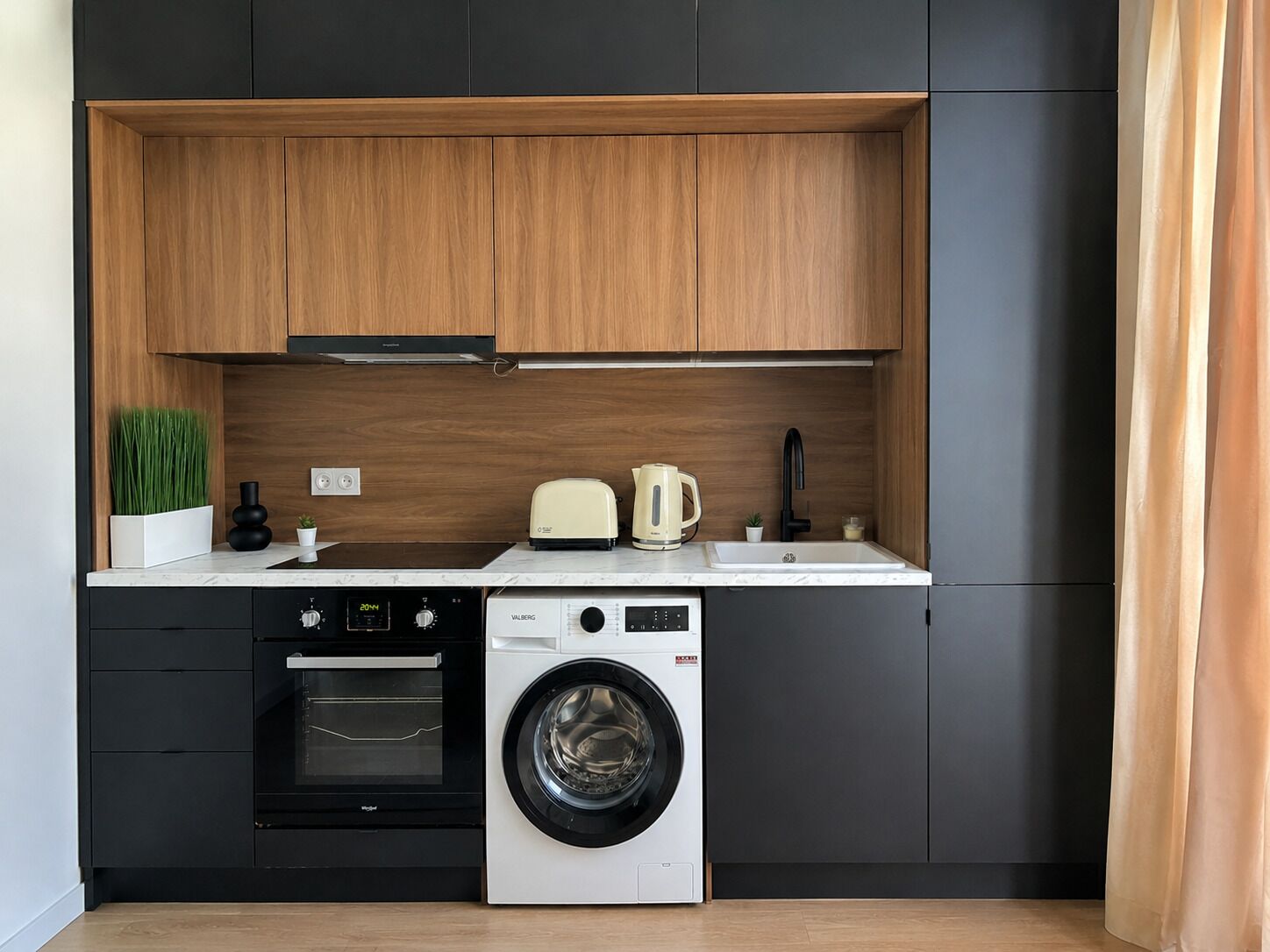 Eine kompakte Küche mit Backofen, Waschmaschine, Toaster und Kaffeemaschine.