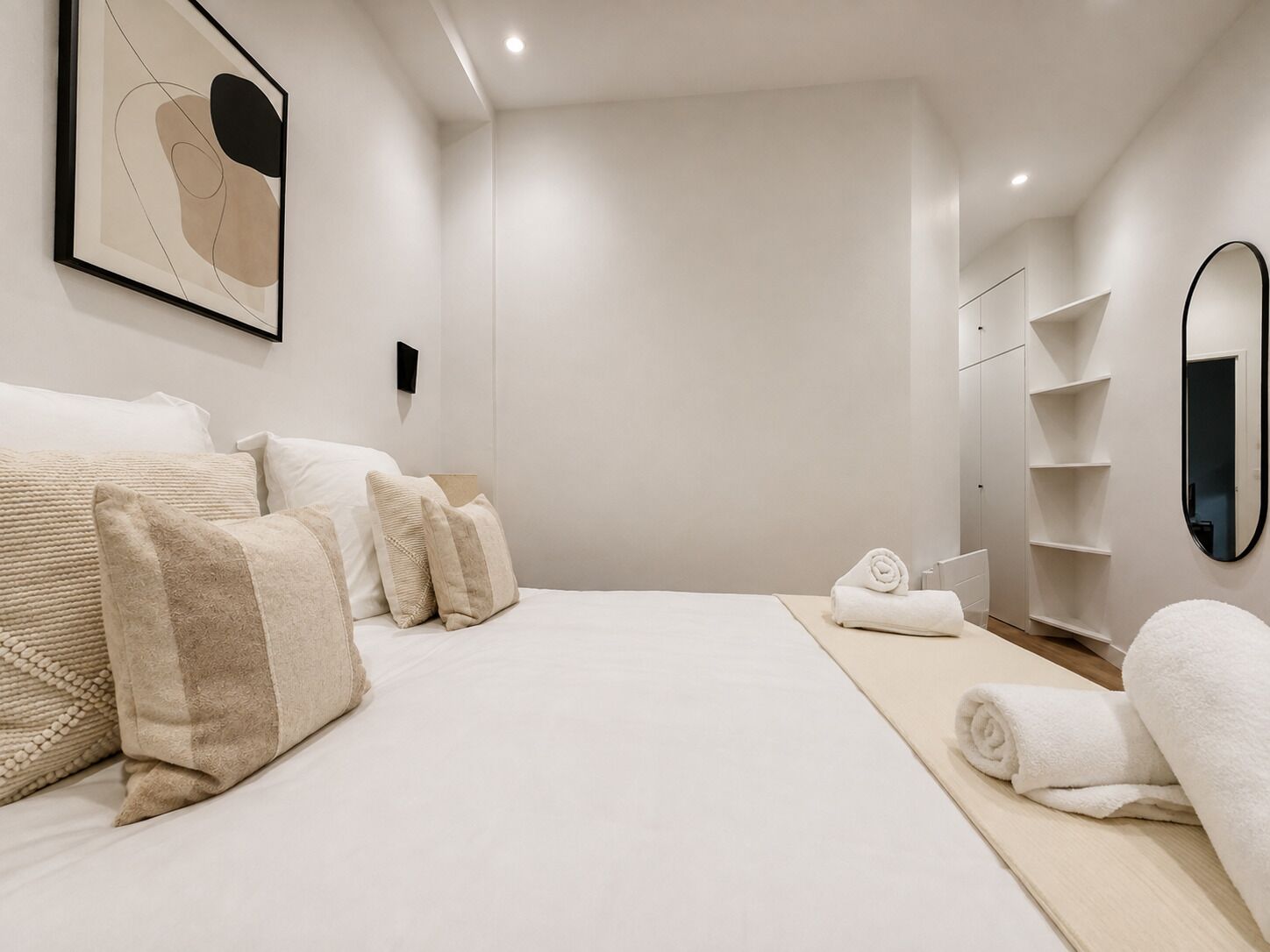 Un dormitorio moderno con una cama grande, una mesita de noche, un espejo y una obra de arte en la pared.