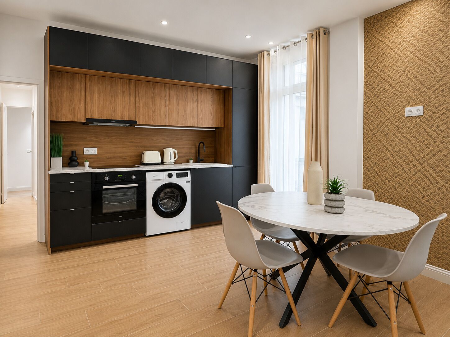 A modern kitchen with a built-in washing machine, a dining area with a round table and chairs, and a herringbone-patterned wall.