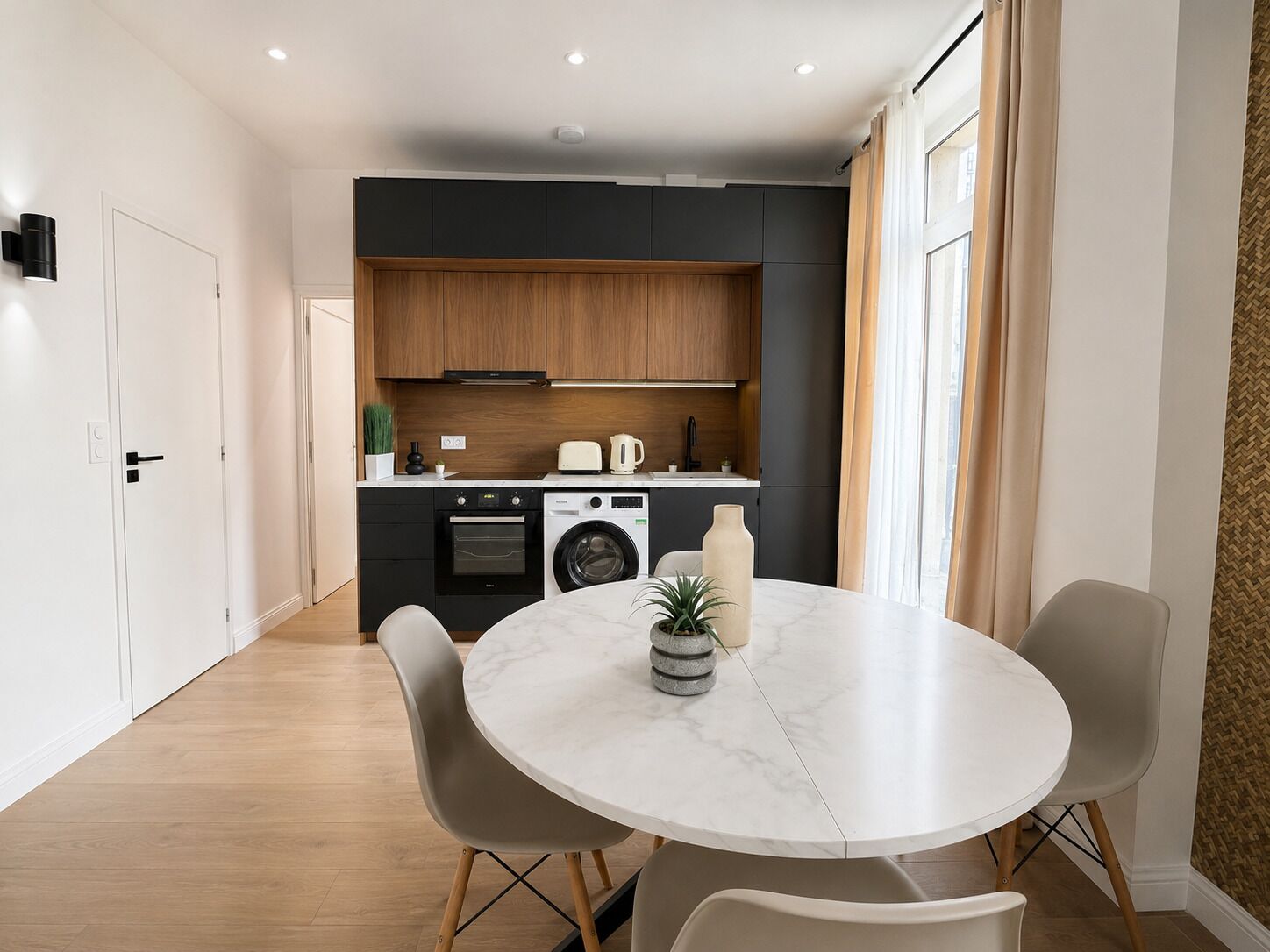 A modern kitchen with a built-in oven, washing machine, and a dining area with a round table and chairs.