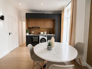 A modern kitchen with a built-in oven, washing machine, and a dining area with a round table and chairs. - Elegant Appartement 2 pieces au 5e  (Paris)