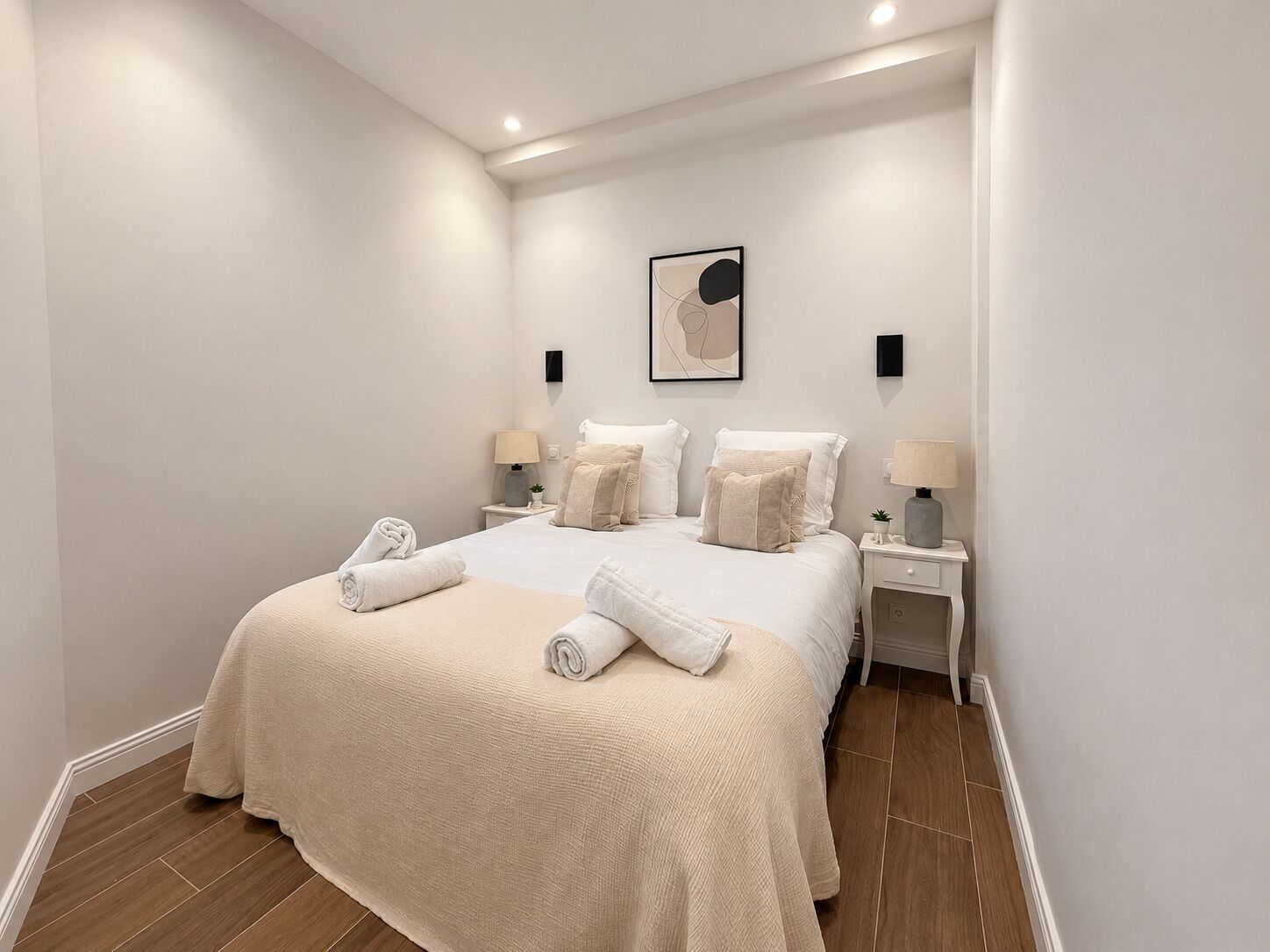 A hotel room with a large bed, two bedside tables, a wall-mounted artwork, and a small potted plant.