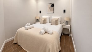 Quarto de hotel com uma cama grande, duas mesas de cabeceira, uma obra de arte na parede e um pequeno vaso de plantas.