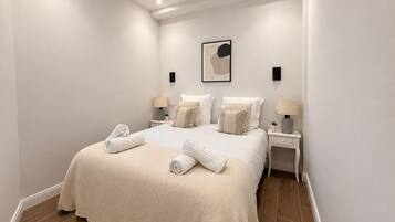 A hotel room with a large bed, two bedside tables, a wall-mounted artwork, and a small potted plant.