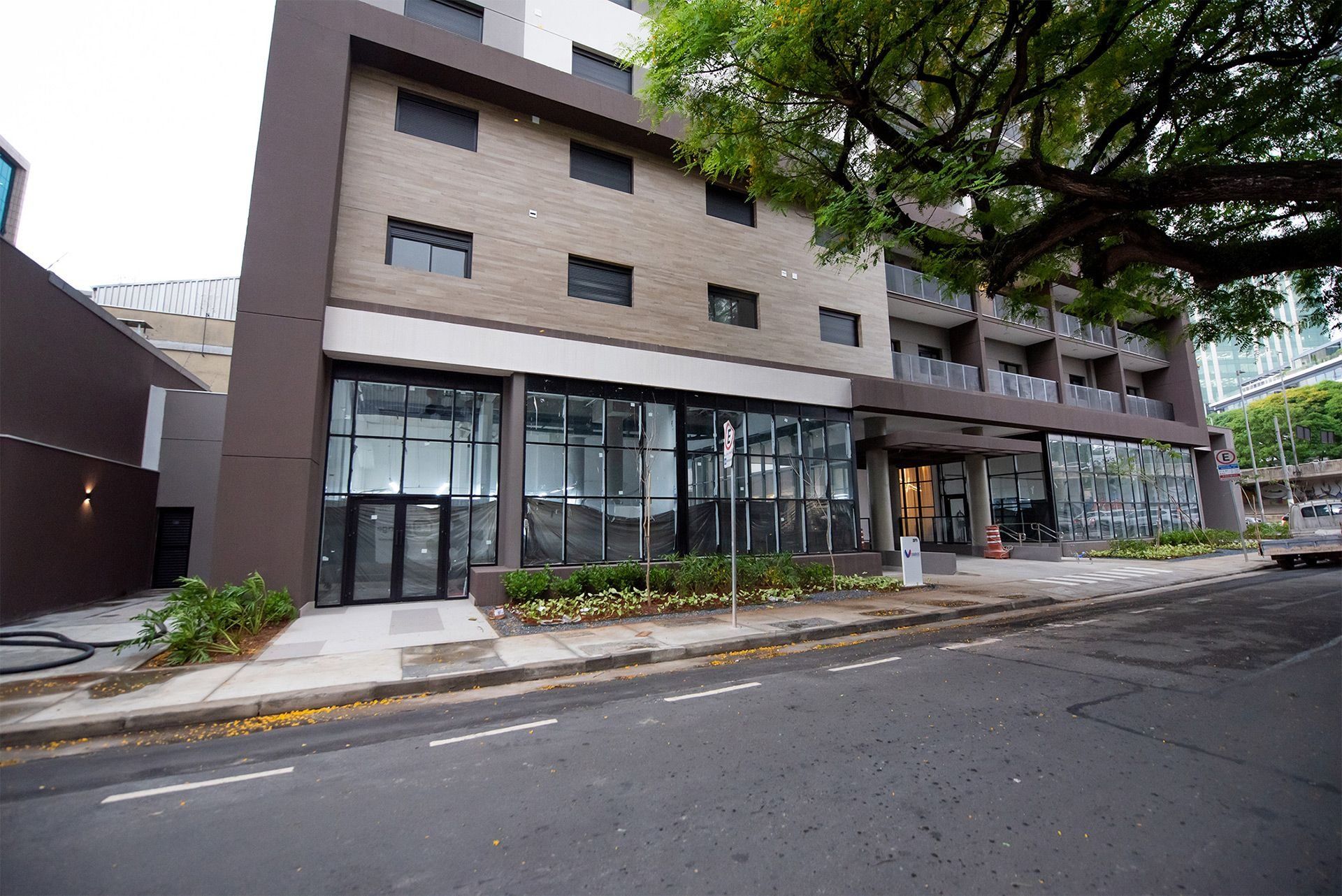 Un edificio moderno con amplios ventanales, un acceso cubierto y un árbol en primer plano.